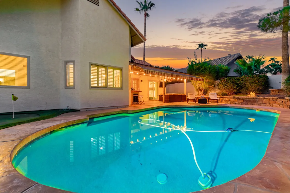 An inviting backyard scene at sunset featuring a sparkling swimming pool, comfortable outdoor seating area, and towering palm trees with a dramatic sunset sky overhead. The space is set up for relaxation and entertaining guests, capturing the essence of private, resort-style leisure.