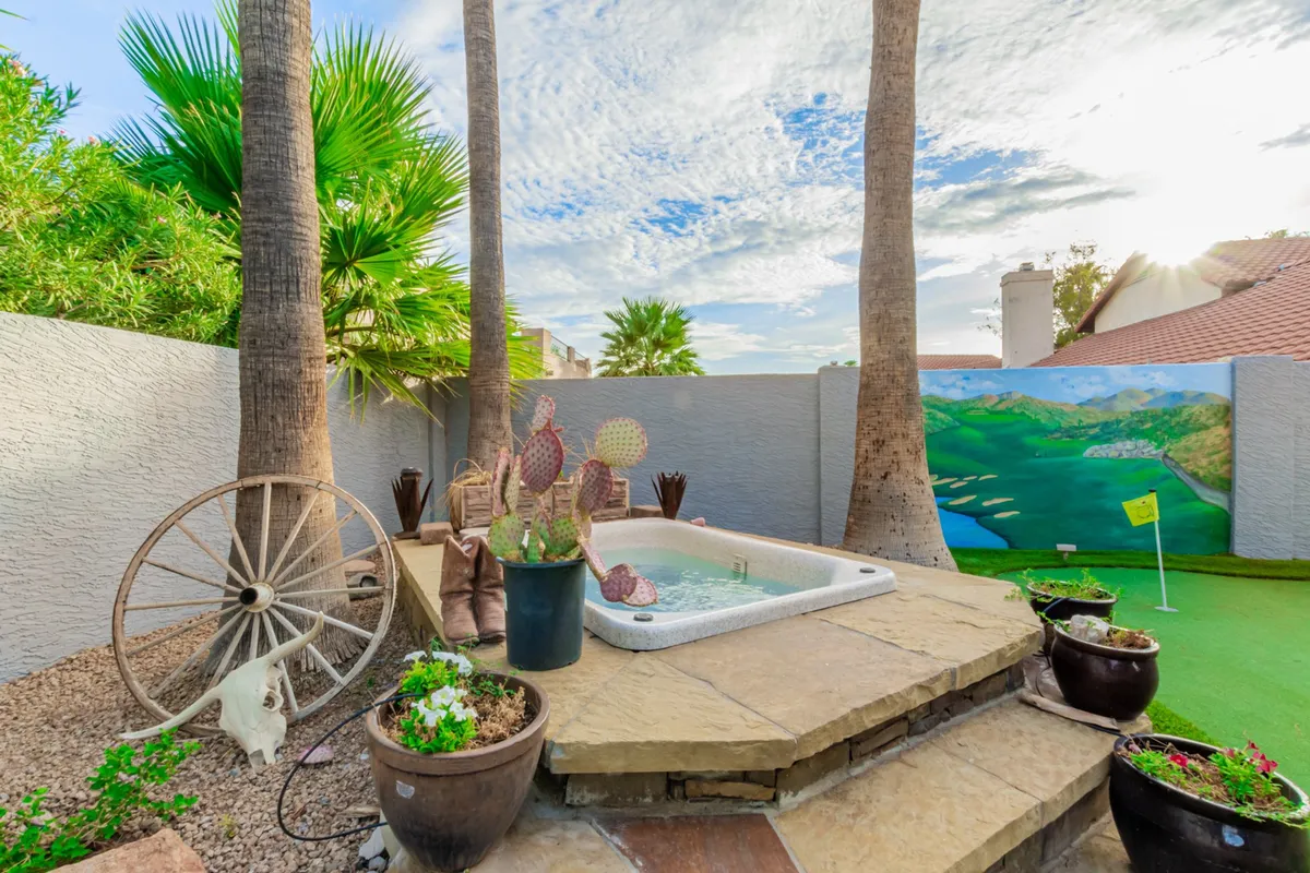 This exterior image captures the backyard jacuzzi surrounded by vibrant cacti, potted plants, a decorative wheel, and prominently features the golf putting green. The tranquil setting exudes a playful, resort-like atmosphere perfect for relaxation and golf practice, with hints of lush landscaping and exclusive amenities.