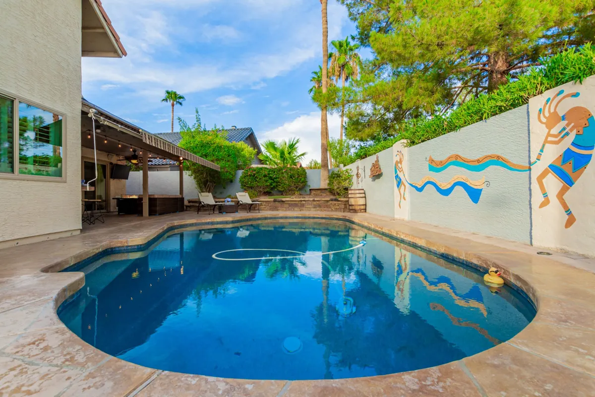A lively, cheerful view of the pool with decorative wall murals, lounge chairs, palm trees, and ample space for gatherings. The scene is set for memorable summer evenings, intimate gatherings, and fun poolside experiences.
