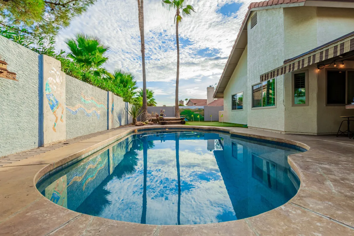 The backyard showcases a sparkling swimming pool surrounded by palm trees and a decorative wall mural, exuding a sense of leisure and fun. The space is ideal for group gatherings, BBQs, and post-event relaxation.