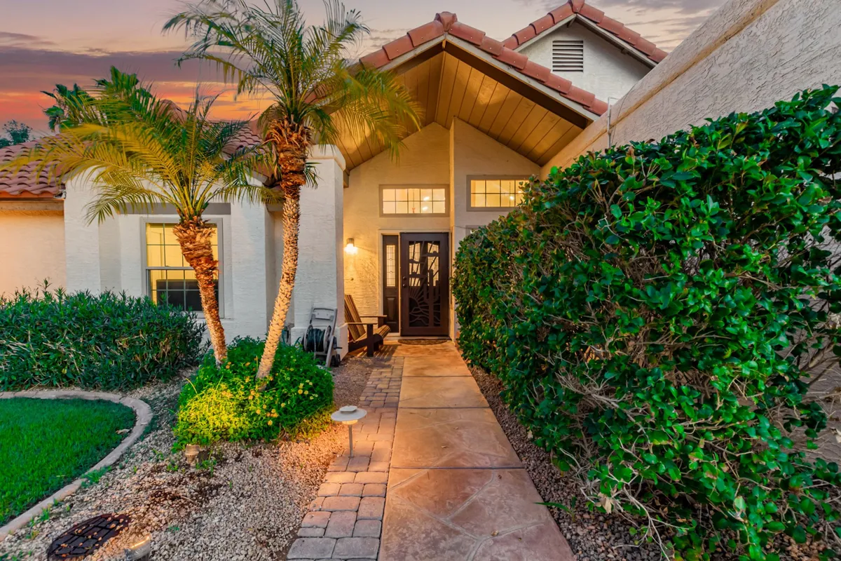 This exterior image features the home's front door framed by palm trees and lush landscaping, with a welcoming pathway leading up to the entrance. The setting is inviting, suggesting an ideal arrival spot for groups gathering before heading out to Scottsdale's major events.