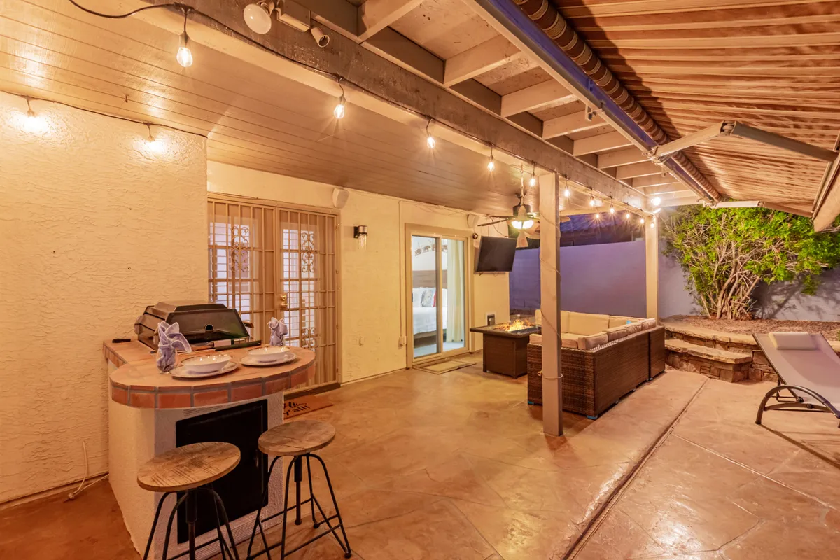 A cozy, stylish outdoor seating area featuring a built-in grill station, strung with twinkling string lights and surrounded by lush landscaping. The scene suggests warmth, comfort, and the perfect atmosphere for outdoor meals or celebrations.