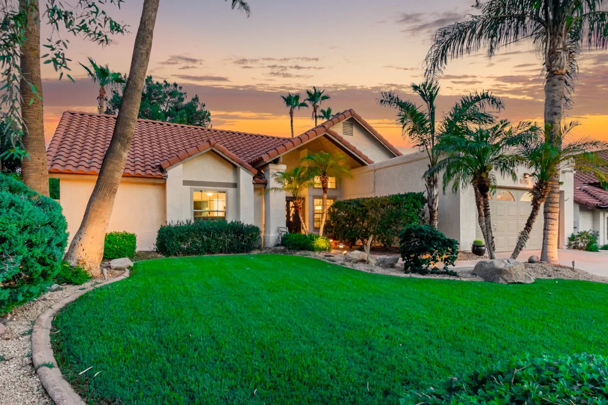 A wide view of the home's front entrance, framed by a lush green lawn, palm trees, and decorative shrubs. The tranquil, inviting mood sets the stage for a welcoming work-retreat experience and hints at the quiet privacy promised for remote productivity.