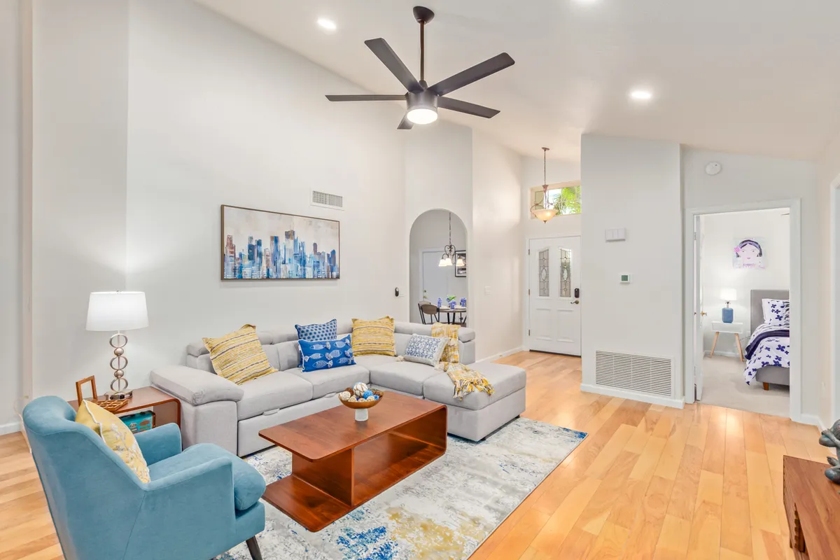 A welcoming open-concept space featuring a plush sofa, modern coffee table, and artwork on the wall. The light fixture above and adjacent dining area highlight the room's airy, communal feel, perfect for gatherings, relaxation, or entertainment.