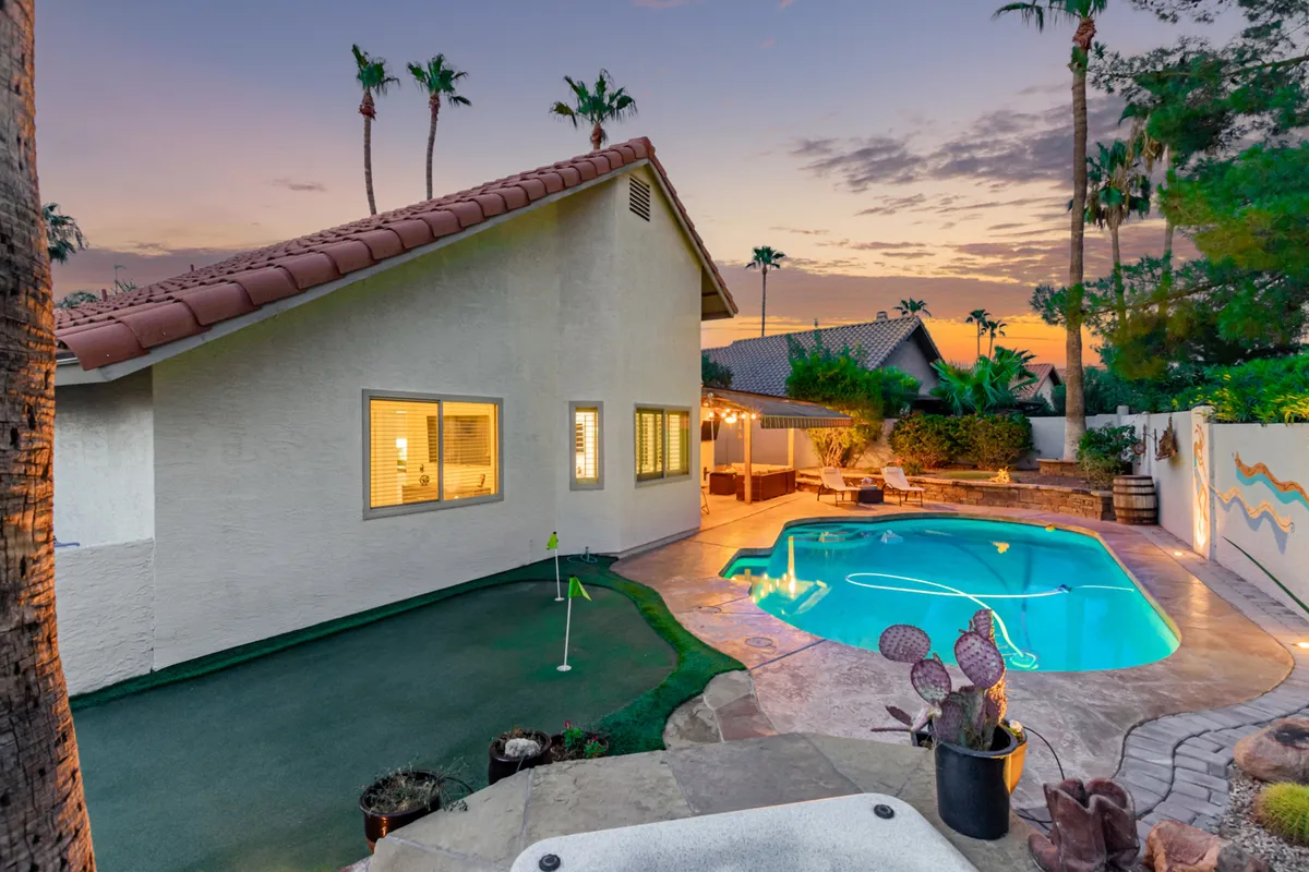 An inviting shot focused on the swimming pool and putting green, with an adjacent outdoor seating and dining area. Palm trees frame the scene, and the evening light hints at magical twilight gatherings. The image communicates both tranquility and social potential.