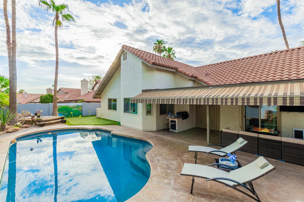 A tranquil pool area with lounge chairs, a spacious patio, palm trees, and a view of the home's exterior. The setting suggests peaceful afternoons spent sunbathing, socializing, or enjoying meals outdoors, all in secluded comfort.