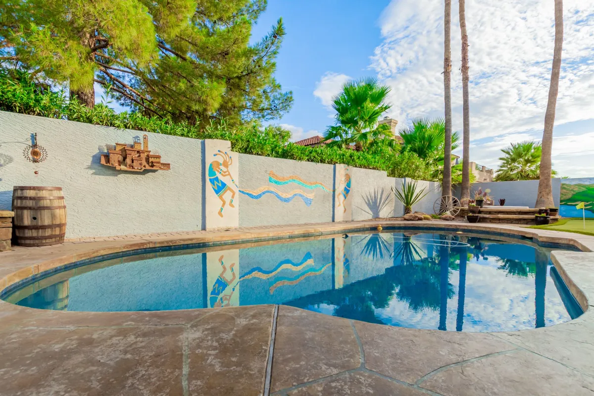 Another exterior shot of the backyard, this image features the swimming pool from a slightly different angle, incorporating the decorative wall mural, palm trees, and hints of a festive atmosphere. It emphasizes areas for sunbathing and outdoor dining.