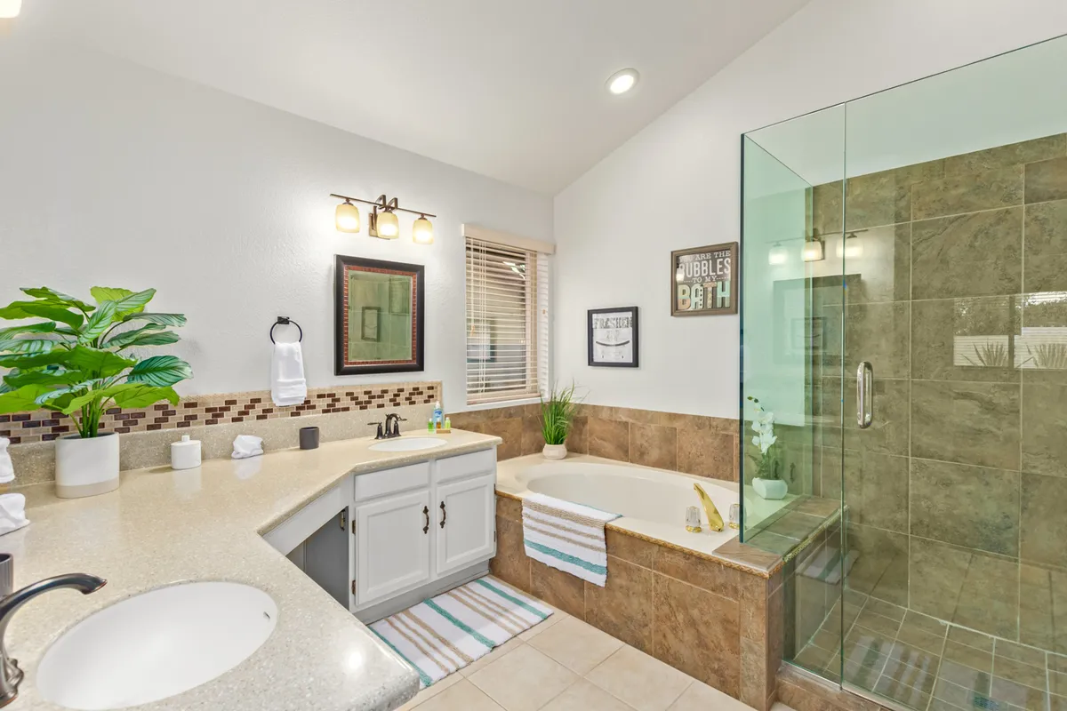 A spa-inspired bathroom featuring a soaking bathtub, glass shower, vanity area, framed wall art, and a lush plant. The space exudes tranquility and offers a luxurious bathing experience.