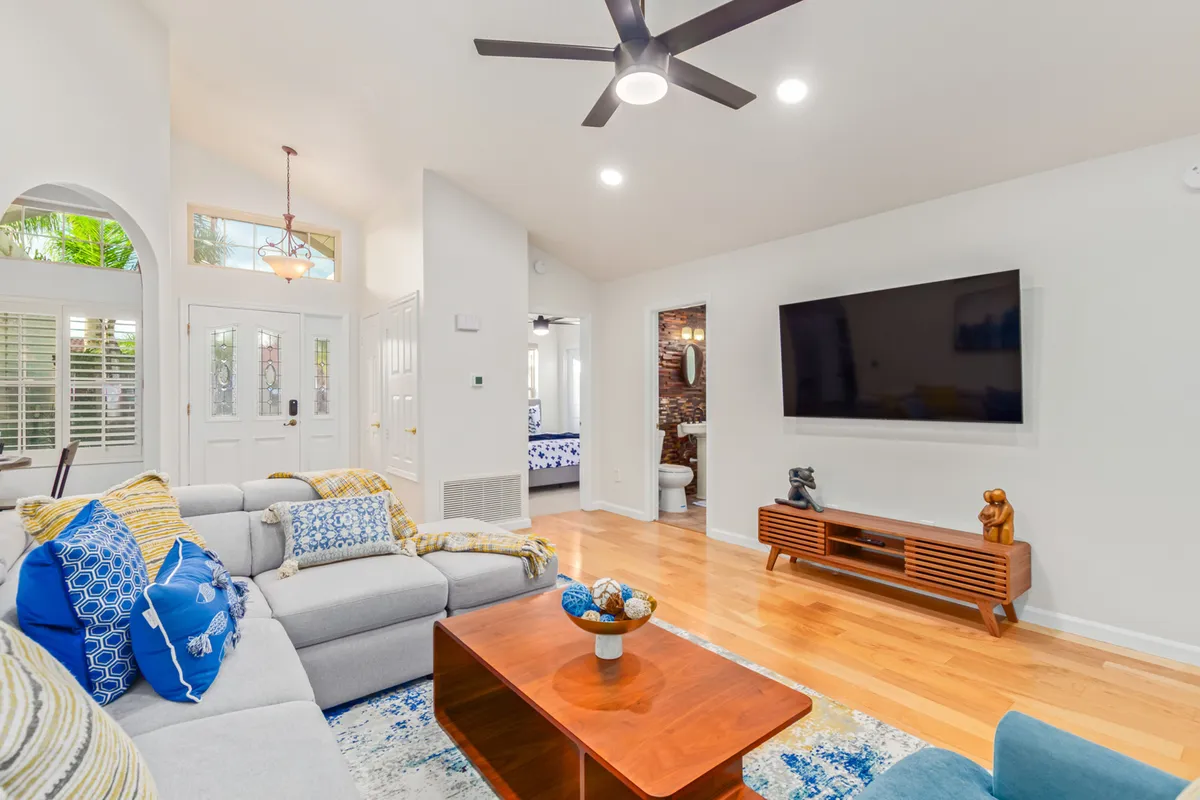 A cozy living space with a wall-mounted TV, blue and yellow accent pillows on a plush sofa, a modern coffee table, and artistic decor. This inviting setup is ideal for movie marathons, reading, or casual conversation.