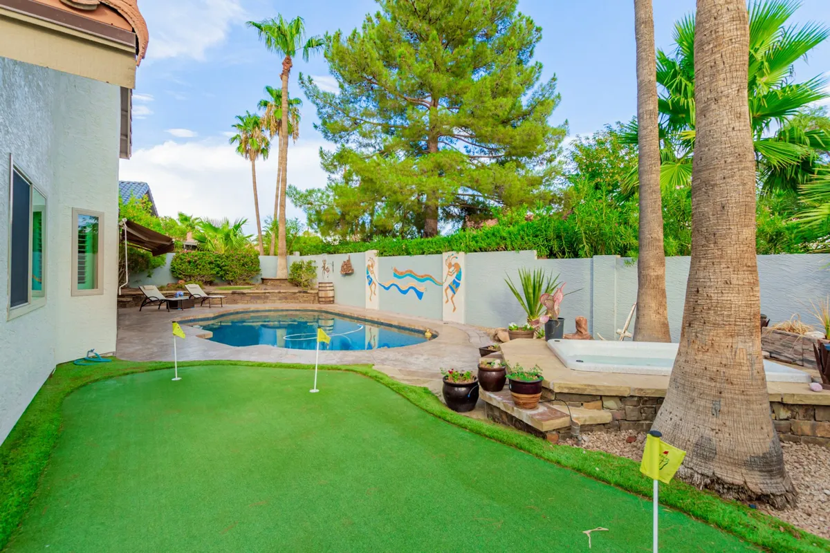 This dynamic exterior shot showcases the swimming pool alongside the backyard putting green, enveloped by palm trees and decorative wall art. The setting invites both active recreation and leisurely downtime, embodying the luxury and fun of a Scottsdale escape.
