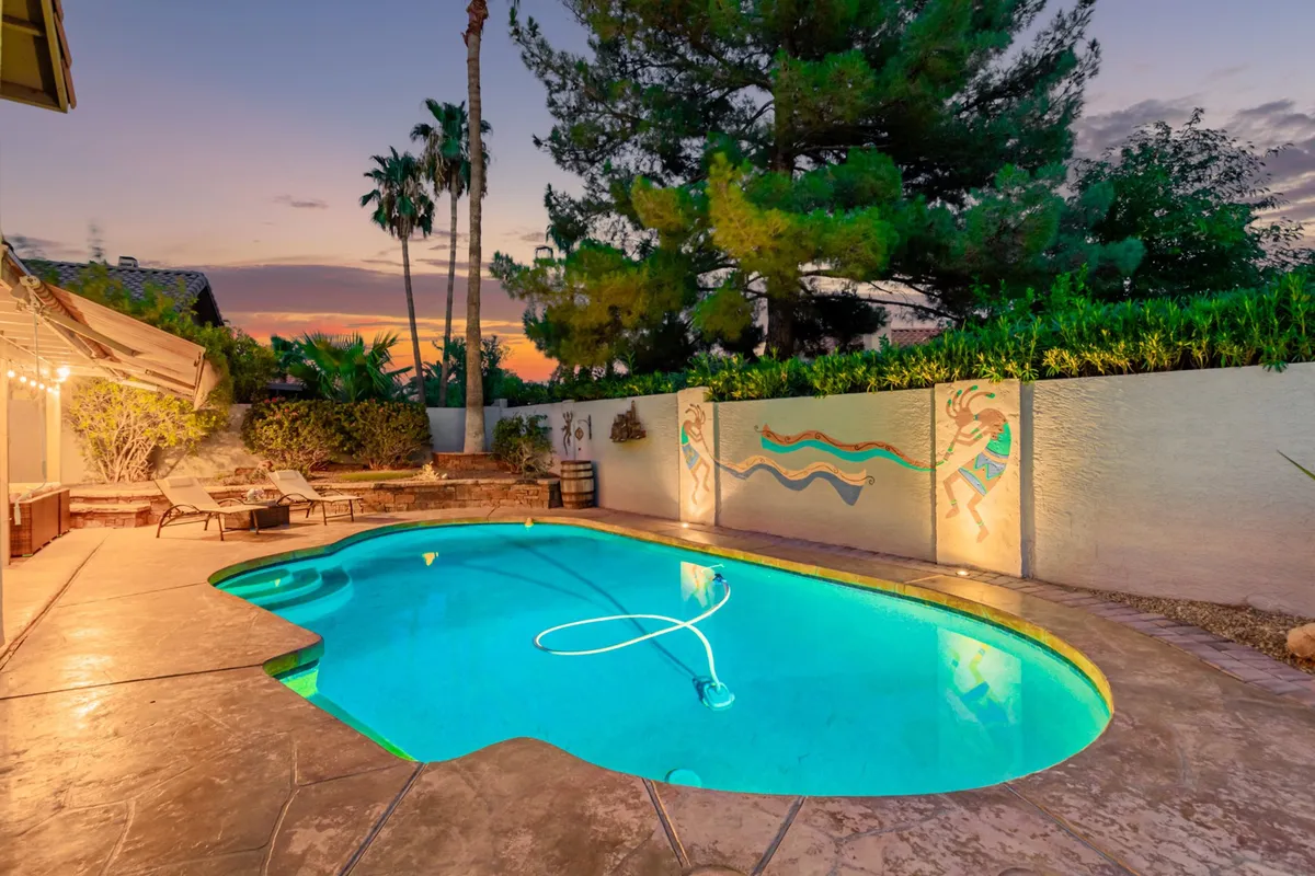 An expansive view of the backyard with a swimming pool, decorative wall mural, landscaped greenery, and a patio area ideal for outdoor dining or evening gatherings. The space is designed for both relaxation and socializing, emphasizing how the home supports a balanced lifestyle.